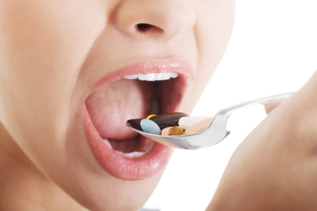 Young woman eating dose of pills on spoon.