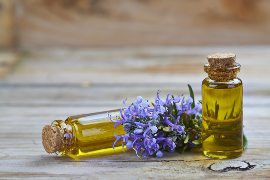 Rosemary essential oil in a small glass vial and plant with flowers on a wooden background
