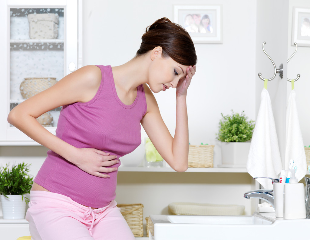 woman with strong pain of stomach and nausea sitting in bathroom
